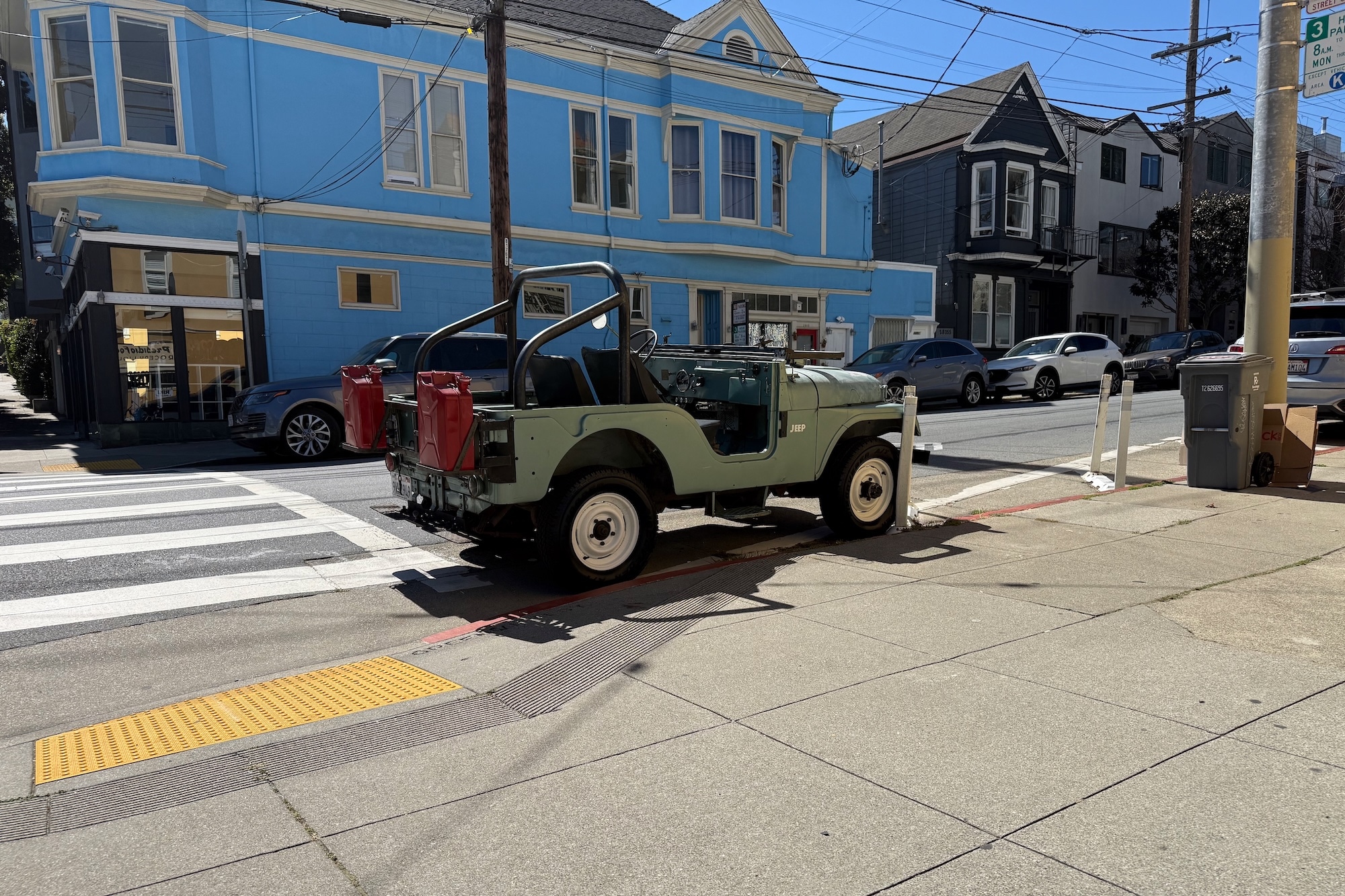 A classic Willys Jeep parked in the street outside of a corner store.