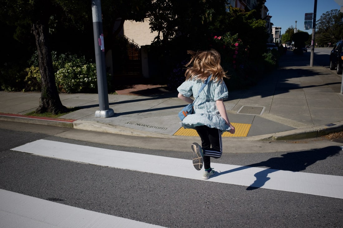 Kiddo jumping on the white stripes that make up a crosswalk.