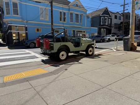 A classic Willys Jeep parked in the street outside of a corner store.