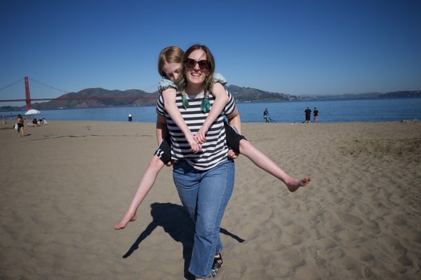 Molly carrying Betty on her back across a sandy beach.